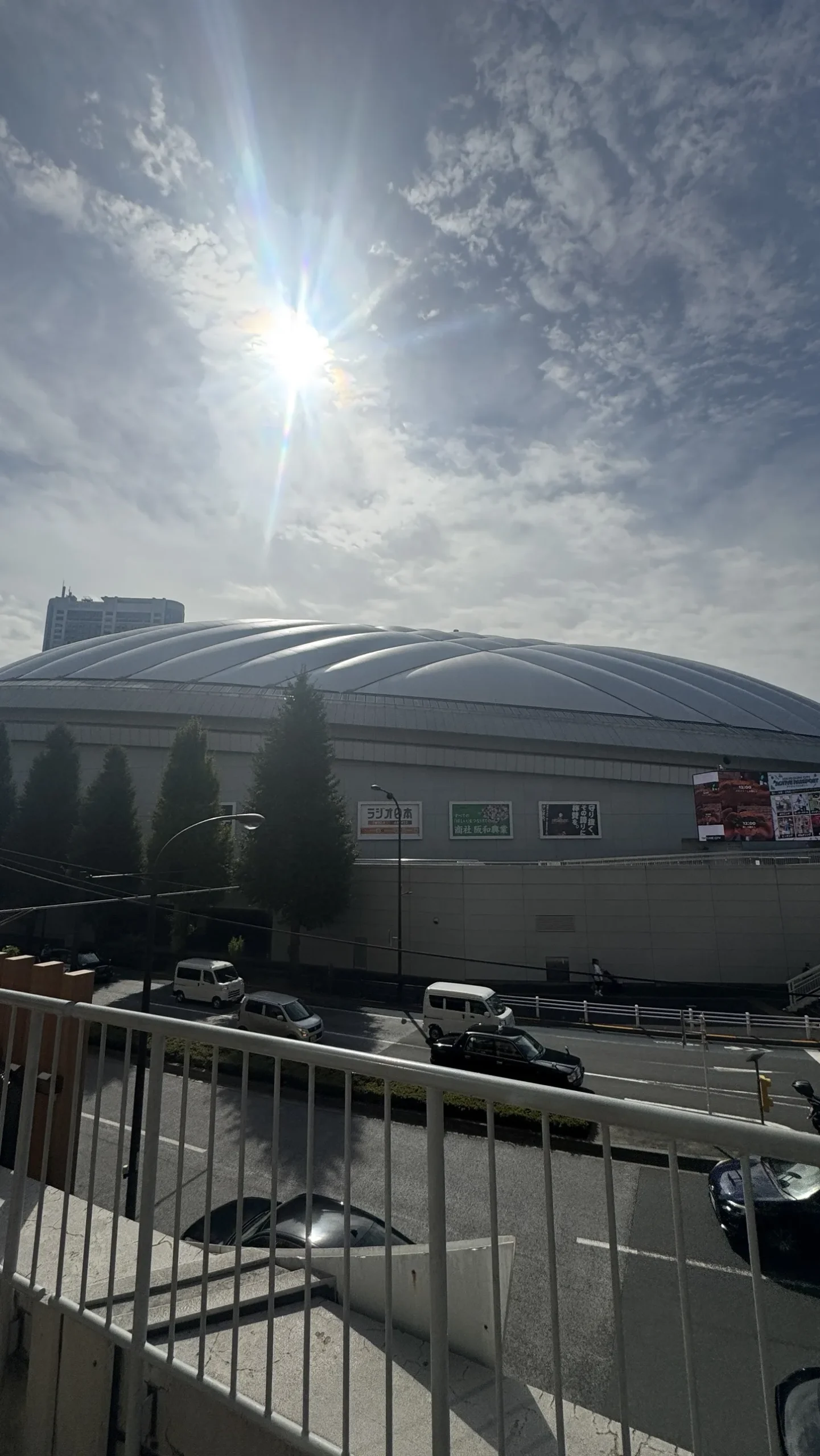 The white roof of Tokyo Dome seen from a pedestrian overpass on a sunny October day, with taxis on the road below
