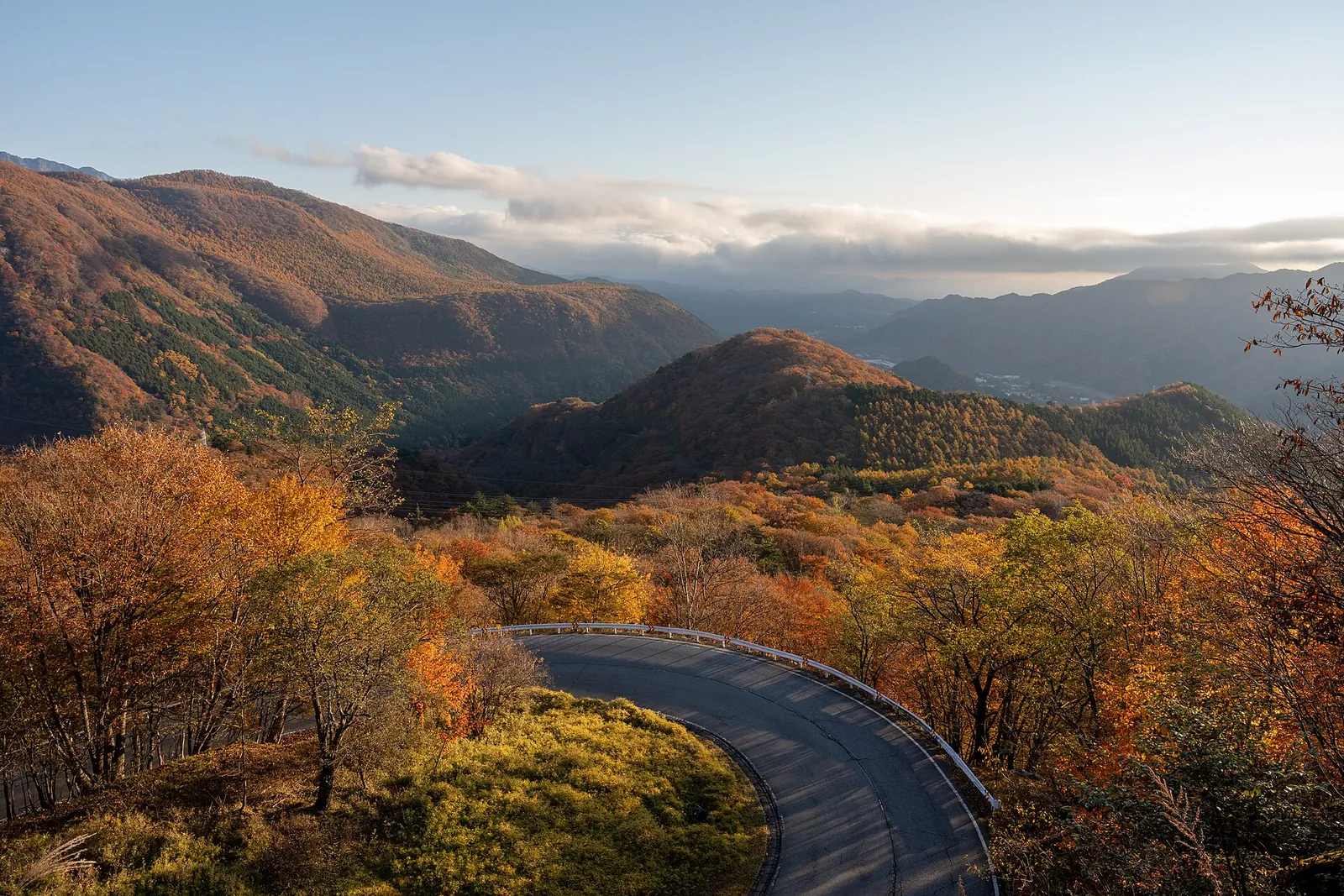 A bend of the Irohazaka road in Nikko curving through autumn leaves, with colored mountains behind it